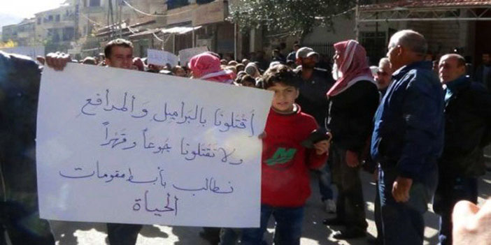  طفل سوري يحمل لافتة في مدينة مضايا