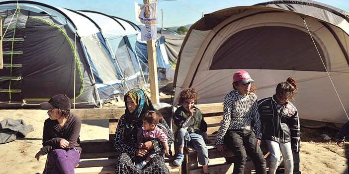  امرأة وأطفالها ينتظرون مصيرهم أثناء جلوسهم في أحد المخيمات المؤقتة في قرية يونانية