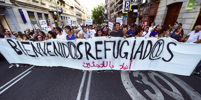  عدد من المتظاهرين في مدريد يحملون لافتات ترحّب باللاجئين