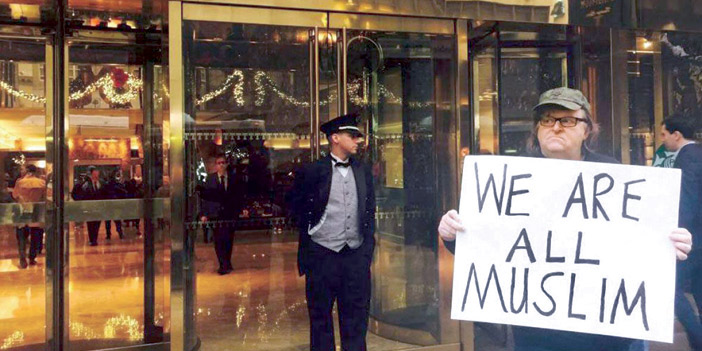  المخرج الأميركي مايكل مور يحمل لافتة كُتب عليها «كلنا مسلمون»، رداً على تصريحات لترامب