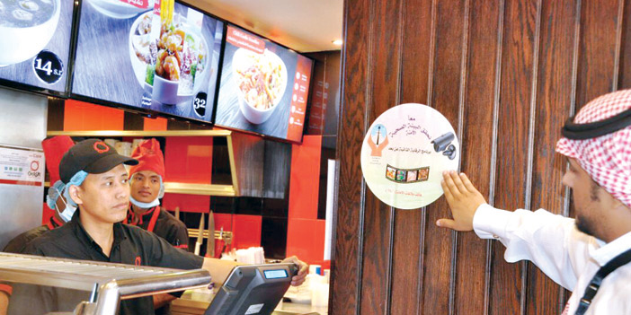  موظف الأمانة يضع ملصق يبين للمستفيدين أن المنشأة خاضعة للمراقبة