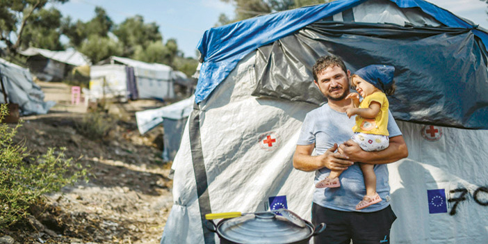  لاجئ سوري يحمل طفلته خارج خيمته الخاصة في إحدى مخيمات اللاجئين