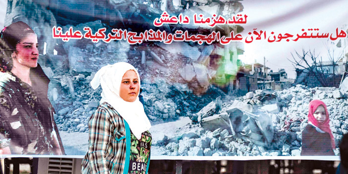  امرأة سورية تتجاوز إحدى اللوحات التي تعبر عن الاعتداءات التركية