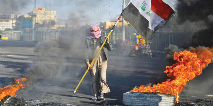  متظاهر يحمل العلم العراقي وسط النيران ببغداد